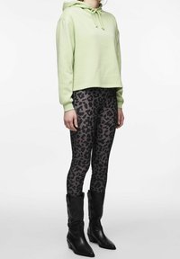 Žena v světle zelené krátké mikině, černých a šedých legínách s leopardským potiskem a černých kozačkách s jehlovým podpatkem do poloviny lýtek.