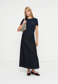 Jūrinės spalvos marškinėliai su širdies dekoru, derinami su ilgu tamsiai džinsiniu sijonu. Aksesuarai - pilka gyvatės odos rašto rankinė ir rudos buteliuko formos basutės.