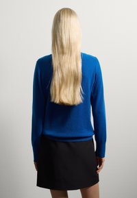 Maglione blu di lana con maniche lunghe, abbinato a una gonna nera. La trama appare morbida e liscia, i capelli sono lunghi e lisci.
