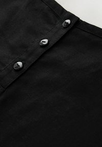 Tissu en lin noir à la texture lisse, avec des boutons noirs distincts le long de l'avant. Design simple et disposition classique des boutons.