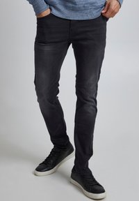 Jeans negros ajustados con una textura suave y un desvanecimiento sutil, combinados con zapatillas negras que tienen una suela blanca.