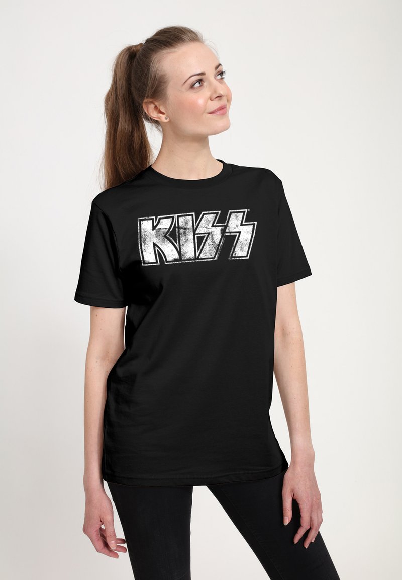 Young woman with long ponytail wearing a black T-shirt with white distressed text "KISS," looking upward with a slight smile.