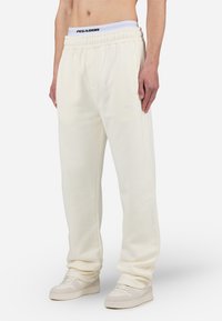 Pantalones de chándal de color crema claro en un material suave, con una cinturilla elástica y bolsillos laterales. Decorados con un detalle del logo en blanco en la pierna.