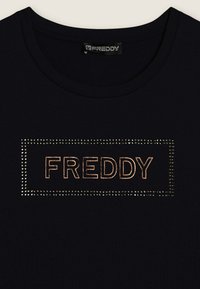 T-shirt noir avec un col rond arborant le mot « FREDDY » en couture bronze, encadré par une bordure de petits clous en argent.