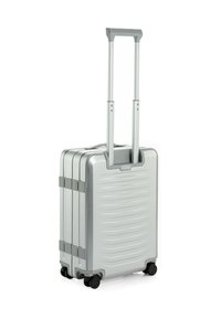 Maleta dura plateada con un acabado texturizado, asa retráctil y cuatro ruedas negras para facilitar la movilidad. Diseño compacto y rectangular.