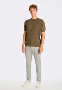 Kortärmad, ribbad, brun stickad tröja med ett texturerat mönster, i kombination med ljusgrå slim-fit byxor och vita sneakers.