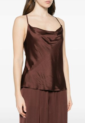 Donna che indossa un top camisole marrone in raso senza maniche abbinato a pantaloni marroni larghi, in piedi su uno sfondo bianco.