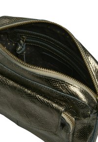 Sac à main gris métallique avec une surface texturée et écailleuse et une fermeture éclair. L'intérieur présente une doublure en tissu foncé avec un motif à pois et des poches.