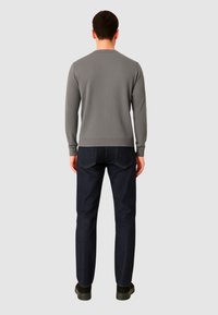 Maglione grigio lavorato a maglia con maniche lunghe, scollo rotondo e polsini a coste, abbinato a jeans in denim blu scuro e calzature nere.