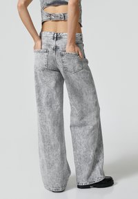Vaaleanharmaat denim-malliset leveälahkeiset farkut, joissa on kulunut kuvio, takataskut ja korkea vyötärö, tyyliteltyinä lyhyen topin kanssa.
