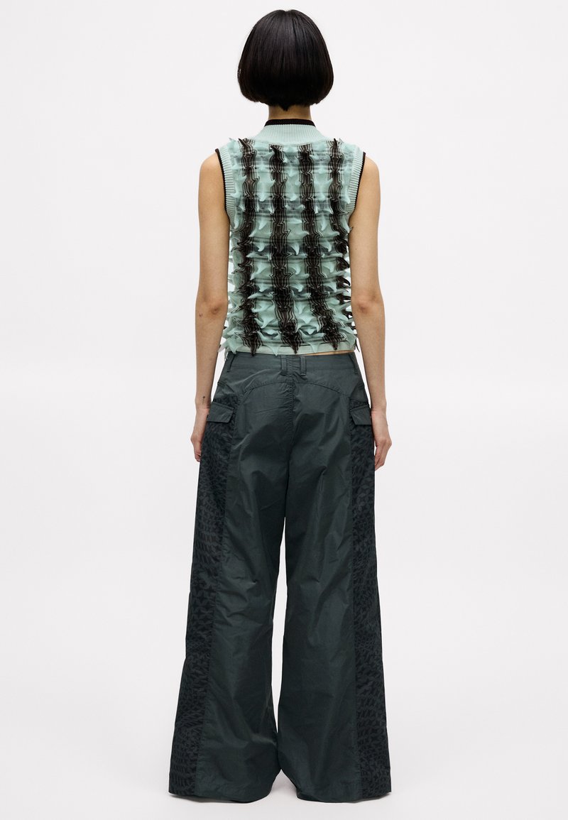 Ljusgrön ärmlös topp med volangtextur och mörkbruna detaljer, kombinerad med överdimensionerade mörka cargo-byxor med mönstrade paneler.
