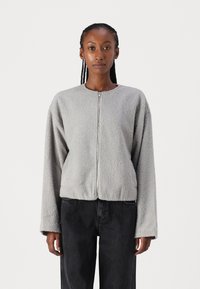 Grå fleecejakke med rund hals, glidelås og lange ermer. Myk tekstur og kort passform, kombinert med mørke jeans.