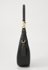 Sac à main en cuir noir avec une forme structurée, doté d'une poignée supérieure et de finitions en métal doré. Comprend une étiquette avec le nom de la marque en relief.