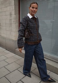 Hnedo-modrý vzorovaný kabát s bielym golierom, spárovaný s tmavými džínovými nohavicami širokého strihu a čiernymi špicatými topánkami, nesúci malú hnedú kabelku.