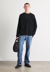 Musta neulemekkokardigan, jossa on viisi nappia, yhdistettynä mustaan T-paitaan ja vaaleansinisiin suoraan leikattuihin farkkuihin. Asusteena pieni musta laukku.