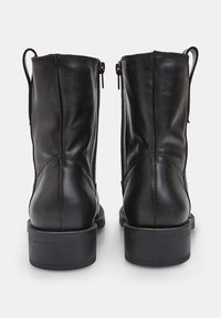 Melnas ādas potītes zābaki ar gludu tekstūru, zemu bloku papēdi un sānu rāvējslēdzējiem. Iekļauj šuvju izšuvumus un vilkšanas cilpas.