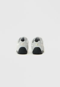 Γκρίζα σουέτ αθλητικά παπούτσια με μαύρη καουτσούκ σόλα, που διαθέτουν μια λευκή ρίγα και ένα μικρό χρυσό λογότυπο στην φτέρνα. Στρογγυλή σχεδίαση στα δάχτυλα.