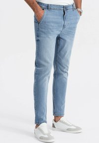 Ljust blå denimjeans med en figurnära design, fem fickor, subtil blekning och knäppning med knappar, kombinerat med vita sneakers.