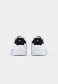 Ein Paar weiße Sneaker mit marineblauen Fersenlaschen, die ein kleines rot-weiß-blaues Logo zeigen, von hinten auf einem schlichten weißen Hintergrund betrachtet.