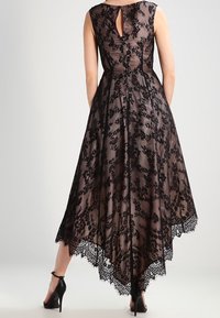 Svart spetsklänning med ärmlöst snitt, nyckelhålsöppning bak och asymmetrisk fåll med scalloped spetskant. Mjukt texturerat överlager.