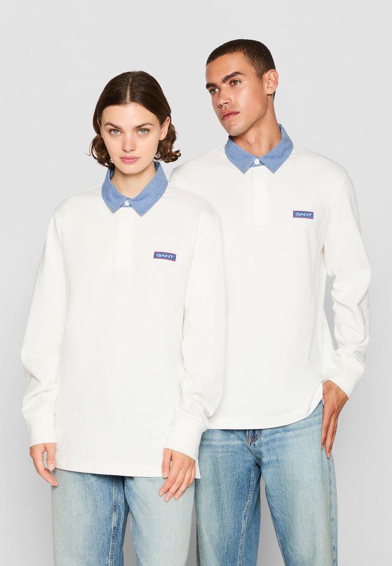 Camisetas polo blancas de manga larga con cuellos estilo denim; cuenta con un pequeño parche de logo azul y rojo en el lado izquierdo del pecho.