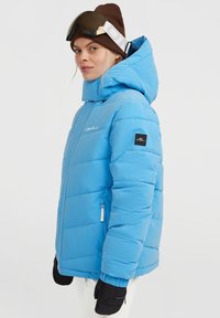 Lichtblauwe gewatteerde winterjas met een hoge kraag, zijzakken met rits en elastische manchetten. Voorzien van logo-accenten en een afneembare capuchon.
