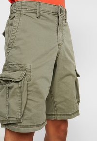 Olivinvihreät, useilla sivutaskuilla, vetoketjullisella etukappaleella ja vahvistetulla ompeleella varustetut cargo-shortsit. Valmistettu kestävästä puuvillamateriaalista.