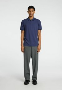 Polo en marine à col zippé, assorti à un pantalon large gris clair et des chaussures noires. Tissu doux avec une coupe structurée.