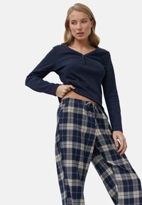 Camiseta de manga larga en navy con dos botones en el escote, combinada con pantalones de pijama a cuadros en navy y crema. Tela suave, corte relajado y cinturilla con cordón.