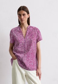 Kurze Bluse mit einem pink-weißen Sprenkelmuster, ausgestattet mit einem V-Ausschnitt und einem lockeren Schnitt. Hergestellt aus einem leichten Material.