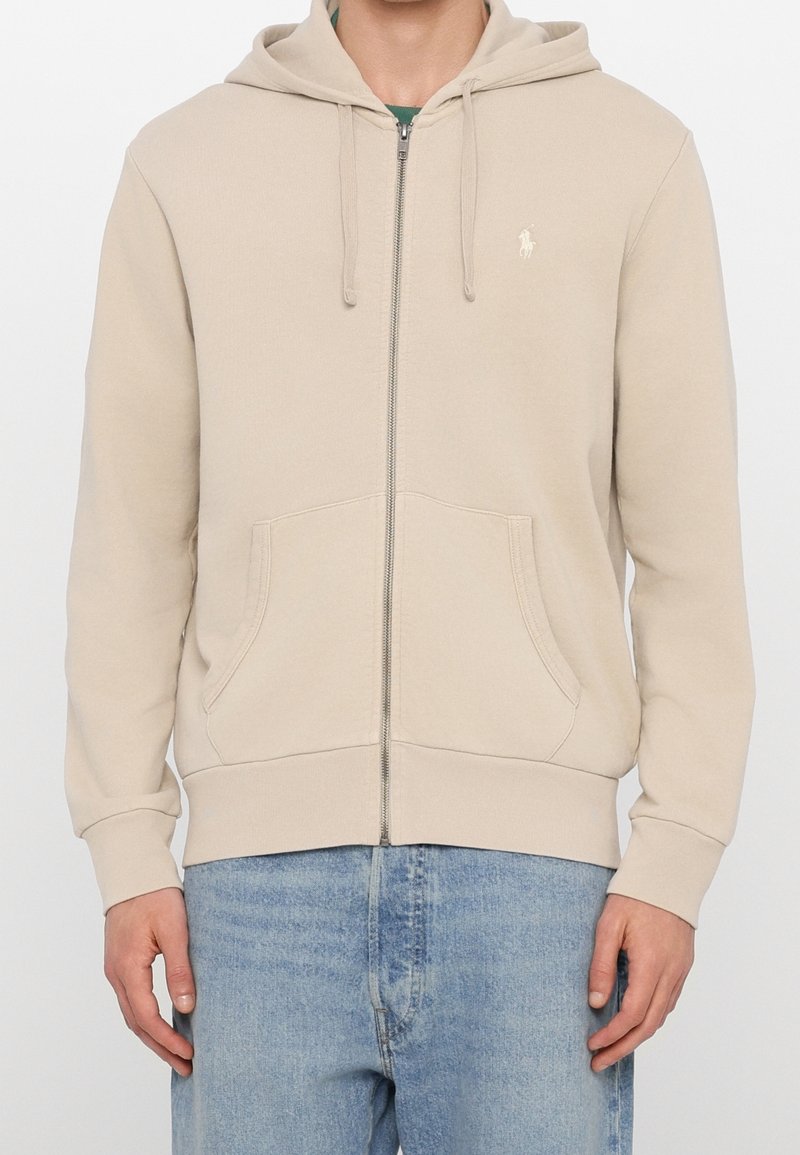 Sudadera con cierre en color beige, hecha de una mezcla de algodón, con un bolsillo tipo canguro, capucha con cordón y un logo bordado en el lado izquierdo del pecho.