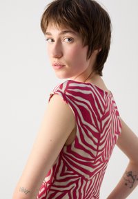 Robe cintrée en tissu rose transparent avec des motifs de feuilles blanches, présentant un col rond et sans manches, révélant les bras et les épaules.