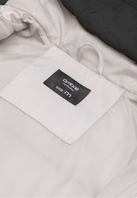 Black and white jacket interior with a tag displaying "ombre," "menswear," and size "M" on a smooth, light fabric background.