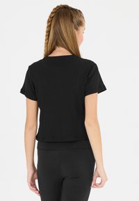 Schwarz, geripptes T-Shirt mit kurzen Ärmeln und einem cropped Design, ausgestattet mit einem Rundhalsausschnitt und einem geraden Saum, getragen zu schwarzen Leggings.