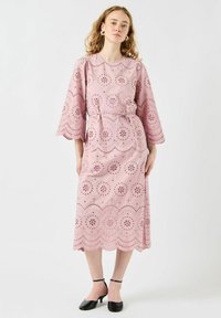 Różowa bawełniana sukienka z wycięciami typu broderie anglaise, z dzwonowymi rękawami do łokci i pasującym paskiem w talii. Zestawiony z falbaniastym wykończeniem u dołu.
