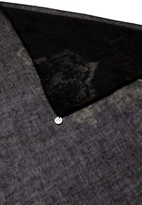 Tessuto di lino nero con superficie texturizzata presenta un design asimmetrico, messo in risalto da un dettaglio in metallo argentato attaccato.