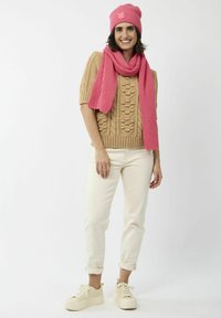 Pull en tricot beige avec un motif texturé, bonnet en maille côtelée rose et écharpe, pantalons blancs et baskets à plateforme crème.
