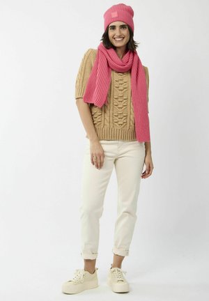 Pull en tricot beige avec un motif texturé, bonnet en maille côtelée rose et écharpe, pantalons blancs et baskets à plateforme crème.