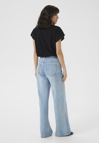 Black short-sleeve top with eyelet details, paired with light blue wide-leg jeans. The outfit features a relaxed fit and a simple design.