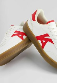 Vita sneakers med röd accent och logotyp, med en slät läderovandel, snörstängning och en sula av gummigummi.