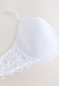 Reggiseno imbottito bianco con dettaglio in pizzo lungo il bordo inferiore e spallina regolabile su sfondo chiaro.