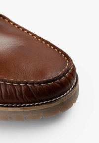 Parte superior de zapato de cuero marrón con punta redondeada, costuras contrastantes y detalles texturizados a lo largo del borde, con suela de goma.