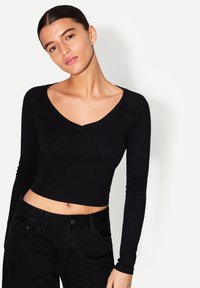 Svart långärmad croptop med djup V-ringning, tillverkad av mjukt material. Designen har en figurnära silhuett och jämn textur.