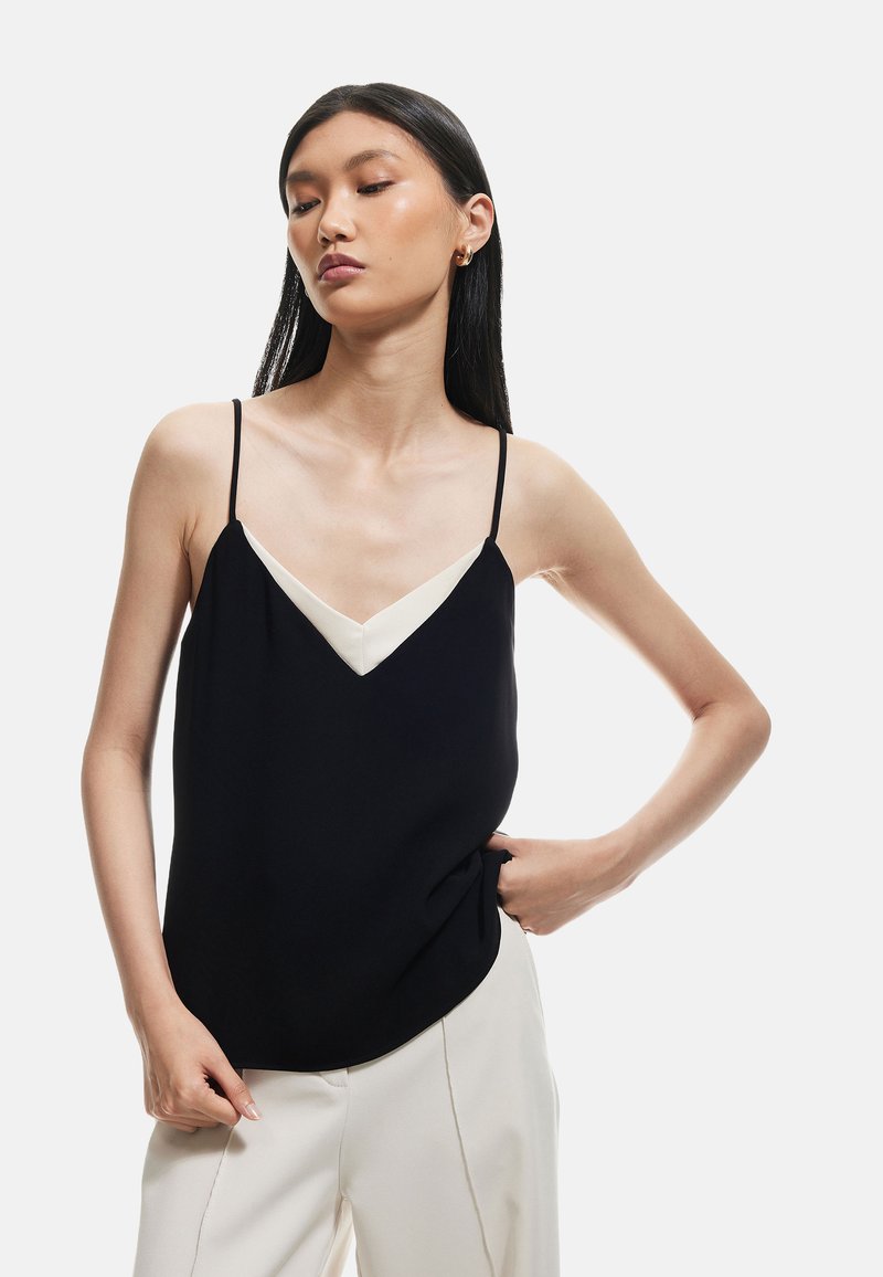 Camisola nera con spalline sottili e un colletto a V di colore crema in contrasto. Il tessuto appare morbido con una vestibilità rilassata, esaltando la silhouette.