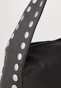 Black faux leather bag with a textured finish. Features silver circular studs along the strap, highlighting its design and detailing.