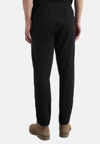 Black sweatpants with an elastic waistband, slim fit, and a back pocket. Material appears soft with a smooth texture. Casual design.