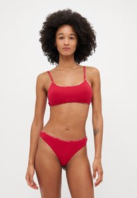 Rød bikini-sett laget av glatt stoff; har en bralette-top med tynne stropper og matchende høykutt underdeler med logo-detaljerte midjebånd.