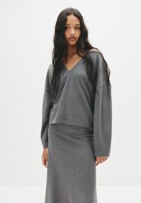 Ensemble en tricot gris comprenant un haut à col en V, des manches longues et une coupe décontractée, associé à une jupe assortie et près du corps. Texture douce sur l'ensemble.