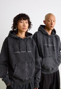 Dideli anglies pilkumo džemperiai su priekinėmis kengūrų kišenėmis, raišteliais ir "ALPHA INDUSTRIES" logotipu. Tekstūruota medžiaga su išblukusia išvaizda.