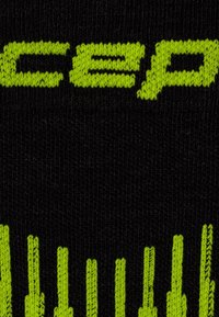 Testo giallo-verde e barre verticali intessute su tessuto nero, che mostrano parte della parola "cep" e un motivo sottostante.